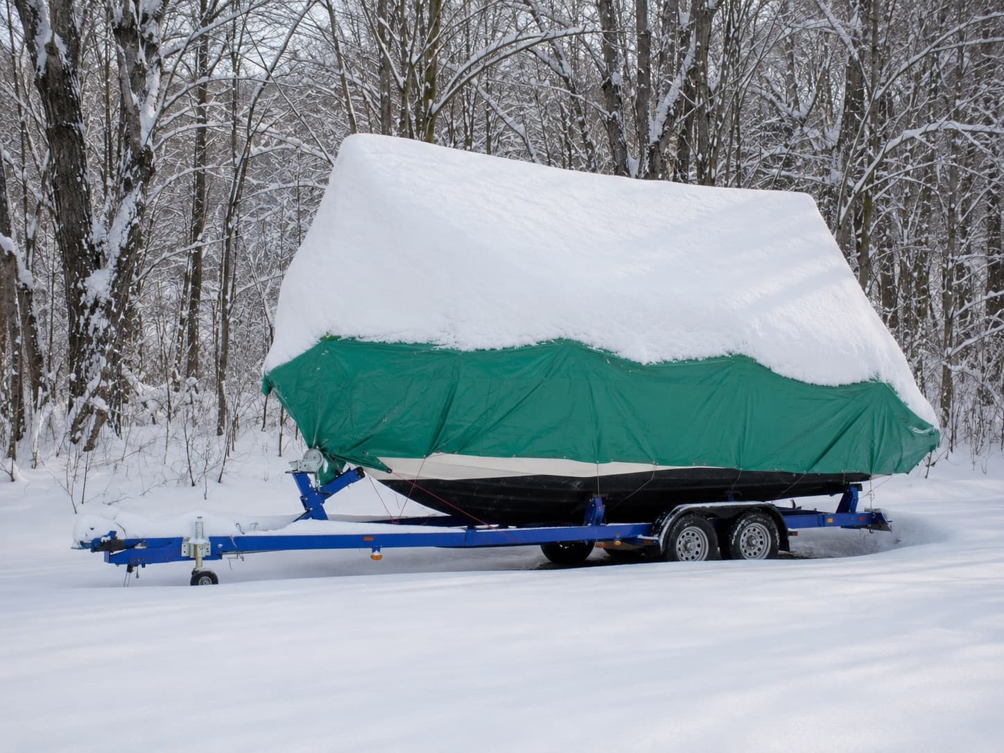 Båt på tilhenger dekket av presenning og snø under vinterlagring